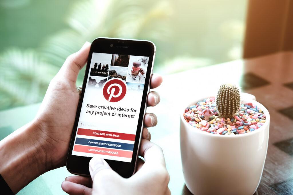 Person's hand holding iphone with pinterest showing how you can utilize the social media app for your material selection meeting